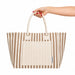Hampton Tote Bag by The Line Edit. - A hand holds a striped brown and cream tote bag featuring a front pocket and dual handles.