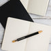 Serenity Aluminium Pen - A black aluminium pen rests on an open cream notebook, with a black notepad also visible in the background.