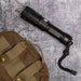 Lumi Rechargeable Torch - A black rechargeable torch placed on a textured grey surface next to a brown tactical bag.