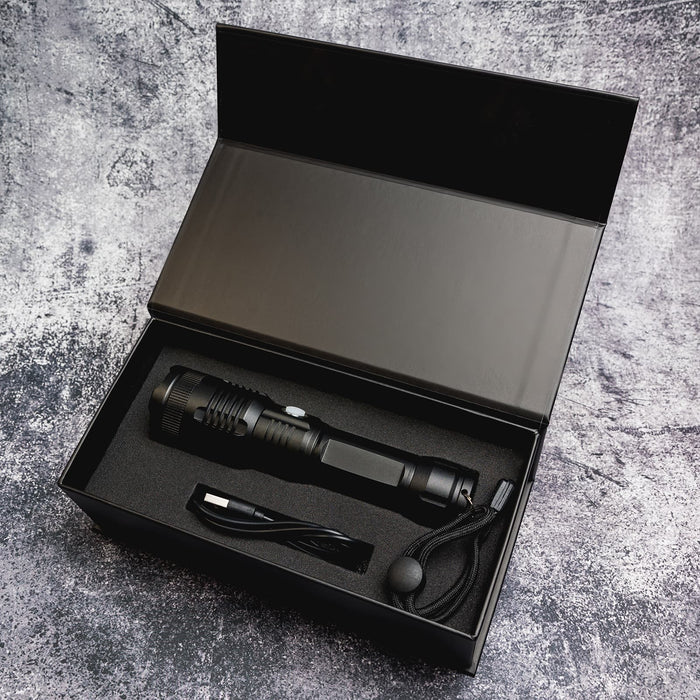 Lumi Rechargeable Torch - A black rechargeable torch with a charging cable, sitting inside a black box with cushioning.