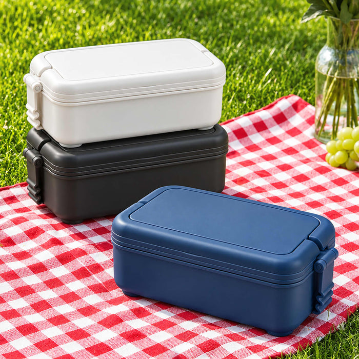 Meridian Double Tray Lunchbox - A stack of lunchboxes in navy, black, and white, sitting on a red and white checkered picnic blanket.
