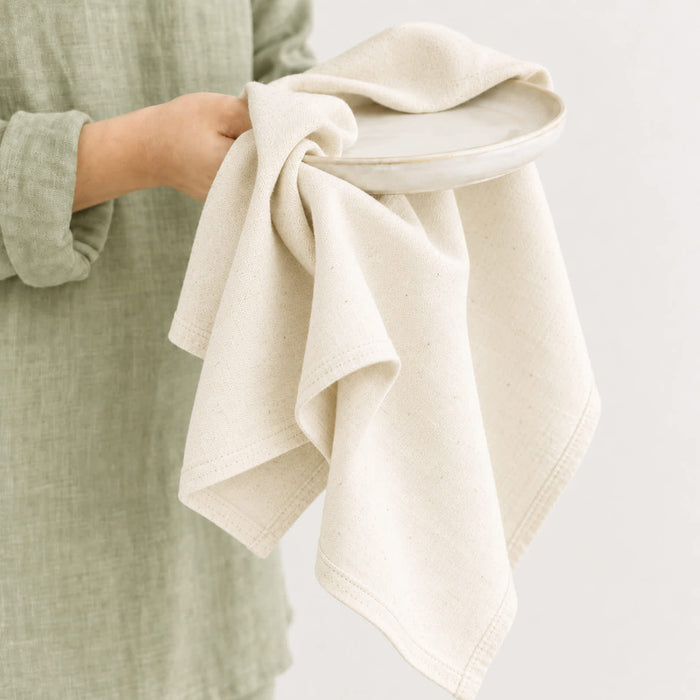 Haven Medium Cotton Tea Towel - A medium cotton tea towel in a natural beige shade held over a ceramic plate, featuring a subtle texture.