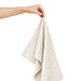 Haven Large Cotton Tea Towel - A hand holds a light beige cotton tea towel, showcasing its soft fabric and folded design.