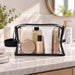 Laynie Clear Cosmetic Bag - A clear cosmetic bag contains various skincare products, including bottles and tubes, with a black trim.