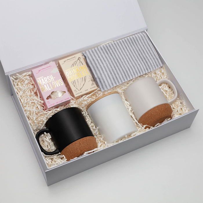 The Warm Welcome - A gift box containing two mugs (black and white), marshmallows, and a striped napkin on shredded paper filling.