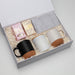 The Warm Welcome - A gift box containing two mugs (black and white), marshmallows, and a striped napkin on shredded paper filling.