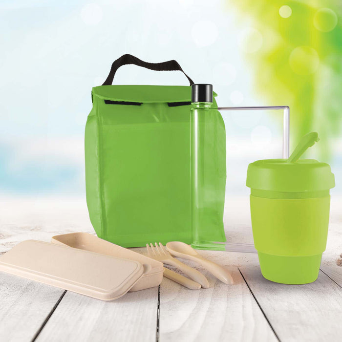 Picnic Pack - A green picnic bag contains a drink bottle, reusable cup, utensils, and food containers, set against a blurred outdoor background.