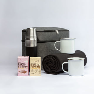 The Winter Warmer Pack - A grey cooler bag with a stainless steel drink bottle, two mugs, a blanket, and boxes of marshmallows and drinking chocolate.