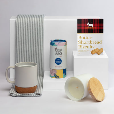 The Brew Ritual - A coffee mug in grey and cork, a tea canister, a candle with a wooden lid, and shortbread biscuits, arranged on a white background.