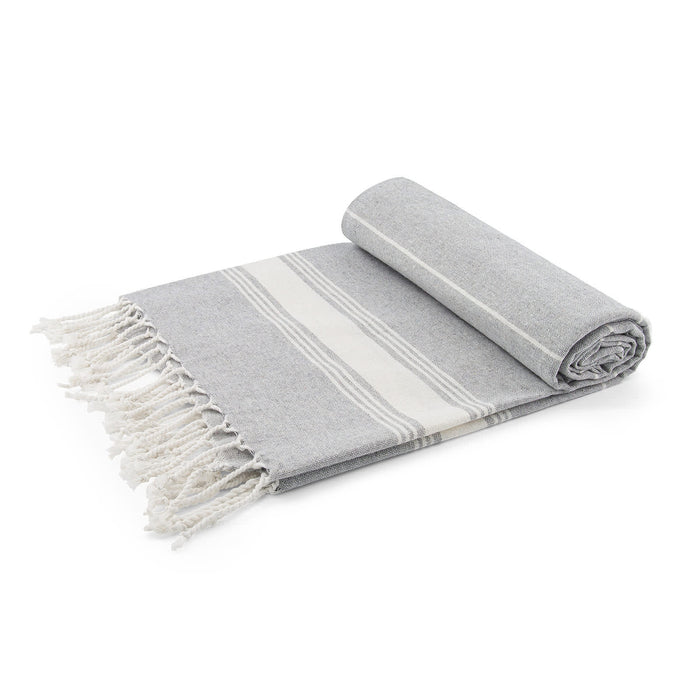 The Sunset Pour - A grey towel with a white stripe pattern and fringed edges, neatly rolled and folded.