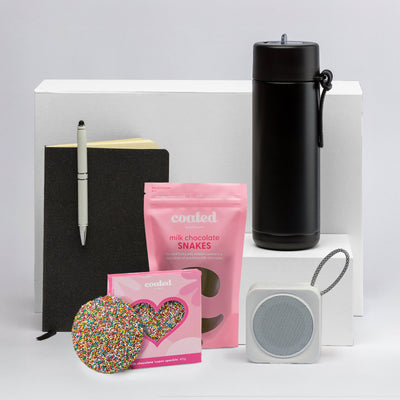 The Sweet Setup - A black drink bottle, notebook, pen, chocolate snakes, a heart-shaped treat, and a portable speaker on a white background.