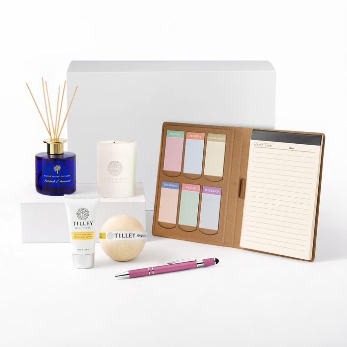 The Mindful Moment - A collection of wellness products including a blue diffuser, white candle, cream lotion, bath bomb, pink pen, and notepad.