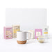 The Cosy Indulgence - A collection of skincare products, a candle, a mug with a cork base, and decorative boxes in pastel colours.