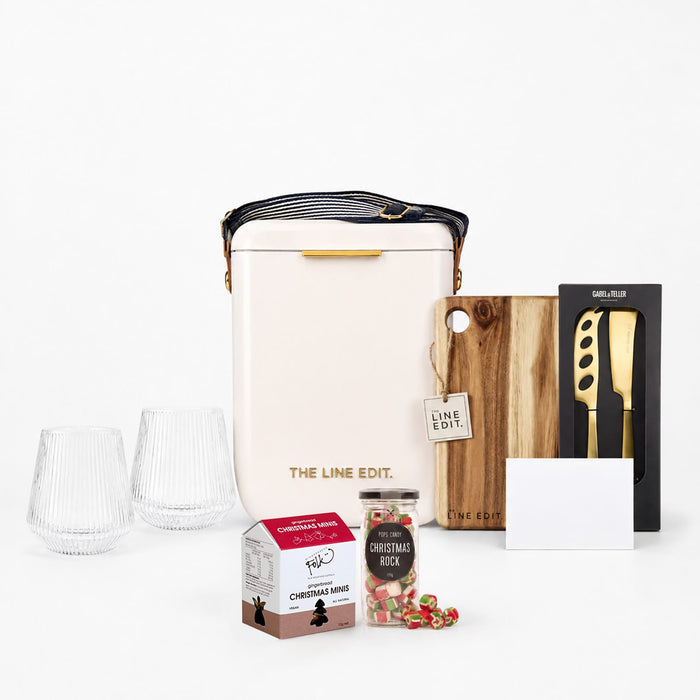 The Festive Edit Gift Set - A cream insulated bag, two clear glasses, a wooden cutting board, a knife, a Christmas treat box, and a card.