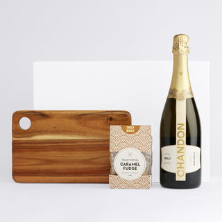 The Sparkling Moment - A drink bottle of sparkling wine, a packet of caramel fudge, and a wooden serving board. The wine bottle features branding.