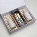 The Pamper & Entertain Edit - A gift box containing two cream bottles and a wooden cheese knife set, arranged on shredded paper.