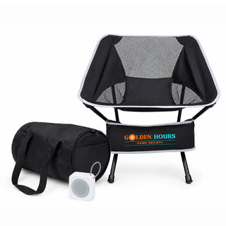The Escape Pack - A portable black camping chair with a mesh back, accompanied by a black storage bag and a small speaker.
