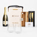 The Pour & Gather Hamper - A champagne bottle, wine glasses, a cutting board, utensils, and a branded cooler in beige and natural wood tones.