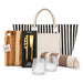 The Weekend Edit - A striped tote bag with a wooden cheese board set, two glass tumblers, and a patterned blanket.