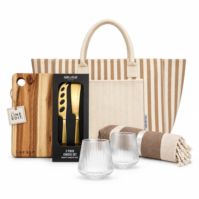 The Weekend Edit - A striped tote bag, a wooden cheese board, a cheese knife set, two clear glasses, and a patterned blanket.