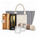 The Weekend Edit - A striped tote bag contains a cheese set, a wooden cutting board, two glass tumblers, and a striped blanket.