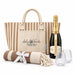 The Sun & Sip Gift Set - A striped tote bag, a champagne bottle, two glasses, and a blanket with a bow, all in neutral tones.