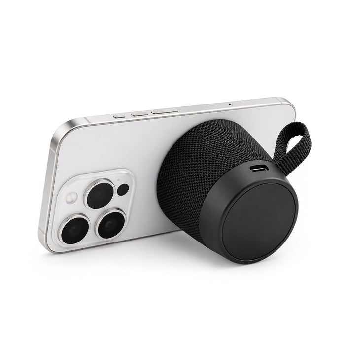 Empire Maglock Ph Stand Speaker - A black, cylindrical speaker with a textured surface, positioned against a smartphone. The speaker has a carrying strap.