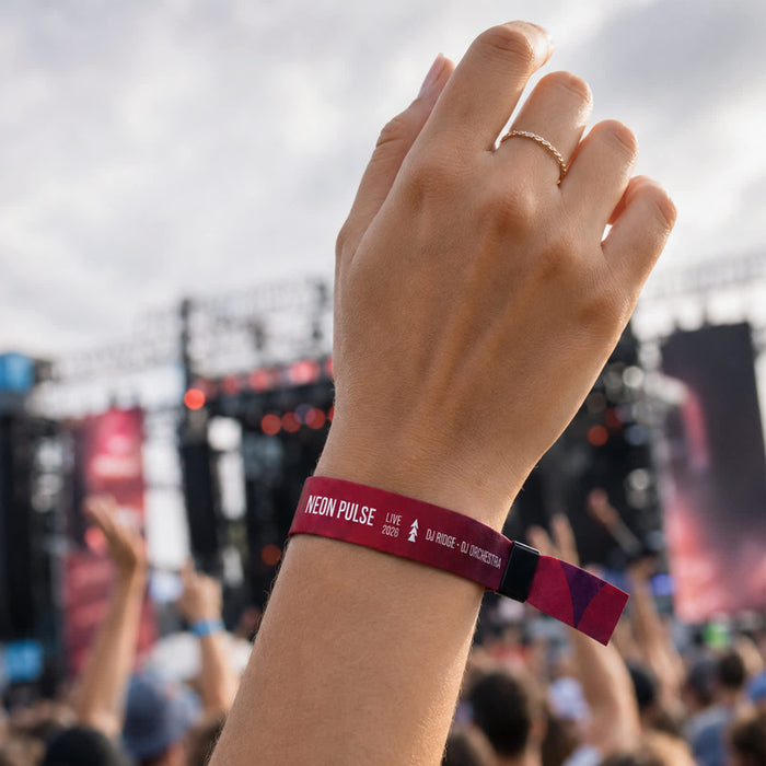 Event Wrist Band - A hand wearing a vibrant pink and purple wristband, with a blurred concert crowd in the background and a stage visible.