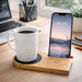Cup Warmer with Inductive Charger - A white mug sits on a bamboo cup warmer with a phone charging beside it. The setting includes a laptop and office supplies.