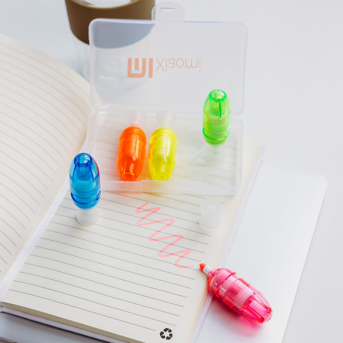 Mackie Highlighter Sets - A transparent case containing four highlighters in blue, orange, yellow, and pink, placed on a notepad with lines.