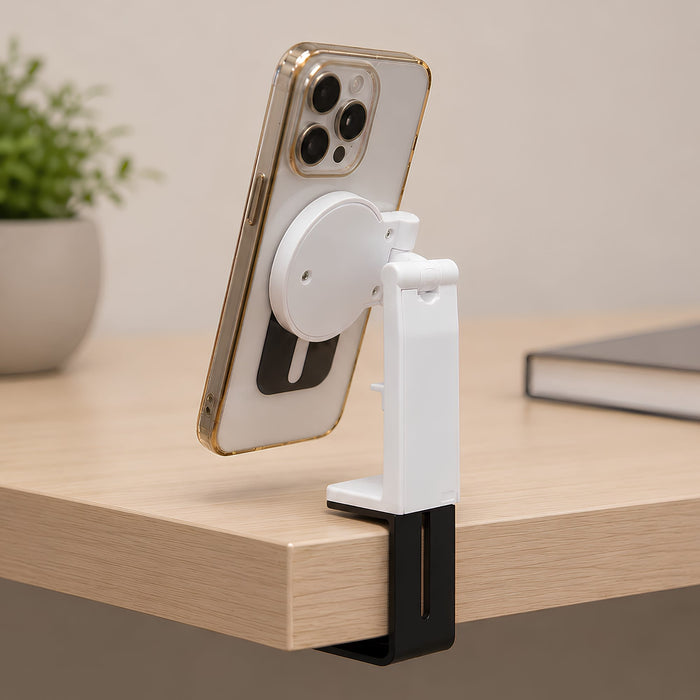 Traveler Mobile Phone Stand - A white and black mobile phone stand holds a phone, attached to a wooden desk. A small plant and a book are in the background.