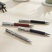 Geneva Metal Pen - A collection of Geneva Metal Pens in grey, maroon, navy, and black with stainless steel accents, arranged on a desk.