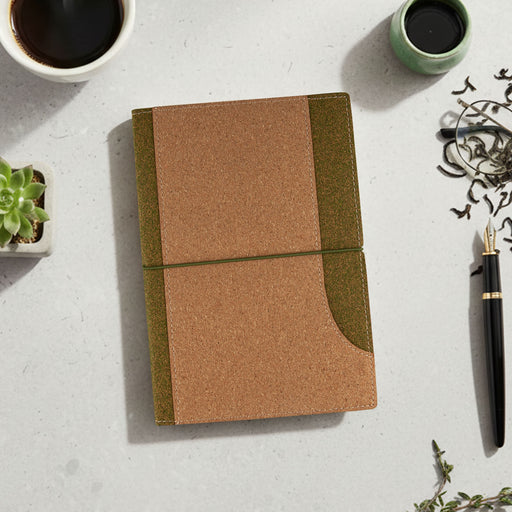 Tea Leaves and Cork Notebook - A cork notebook in brown and green, placed on a light surface with a cup, plant, and pen nearby.
