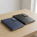 Nexus Notebook - Two Nexus Notebooks in navy and black, each featuring a textured cover and a branding logo, resting on a wooden table.