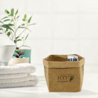 Sewo Kraft Paper Storage Bag – Small - A small brown kraft paper storage bag with a logo, placed beside neatly folded white towels and a green plant.