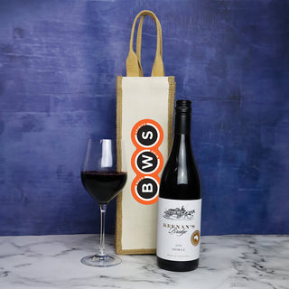 Jute Single Wine Bag - A jute single wine bag in cream with a brown handle, alongside a bottle of red wine and a glass filled with wine.