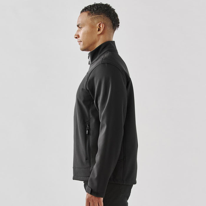 Men's Aleutian Softshell Jacket - A men's softshell jacket in black, featuring a high collar and a side zip pocket. It has a logo on the chest.