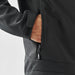 Men's Aleutian Softshell Jacket - A black softshell jacket with a zippered pocket, featuring a hand reaching inside the pocket.