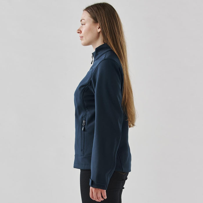 Women's Aleutian Softshell Jacket - A softshell jacket in navy blue, featuring a zip pocket, shown from the side on a model with long hair.