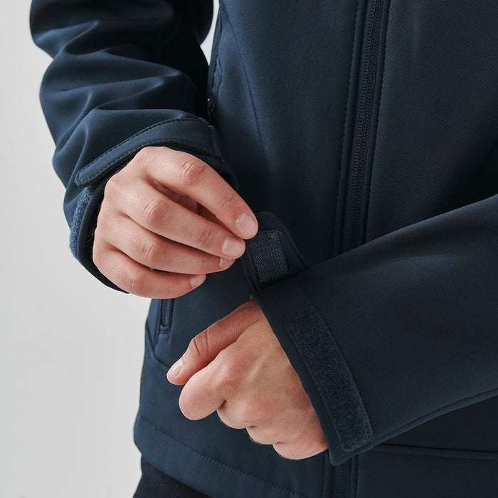 Women's Aleutian Softshell Jacket - A dark blue softshell jacket with adjustable cuffs, featuring a person fastening the wrist strap.