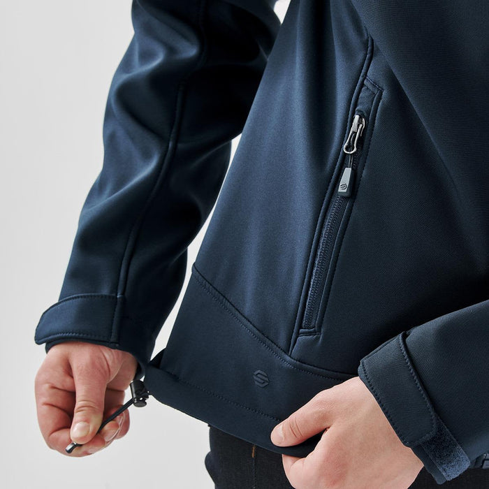 Women's Aleutian Softshell Jacket - A close-up of a women's navy softshell jacket featuring a zipped pocket and adjustable hem. The jacket has a brand logo.
