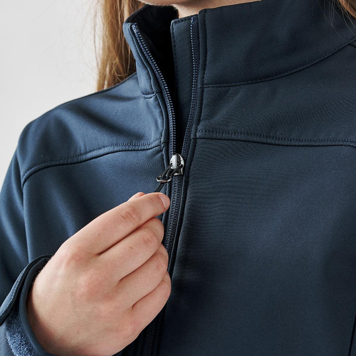 Women's Aleutian Softshell Jacket - A navy women's softshell jacket with a zippered front, featuring a hand adjusting the zipper.