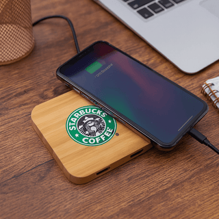 Trafalgar Bamboo charging dock - A bamboo wireless charging dock with a phone on top, featuring a logo and placed on a wooden surface.