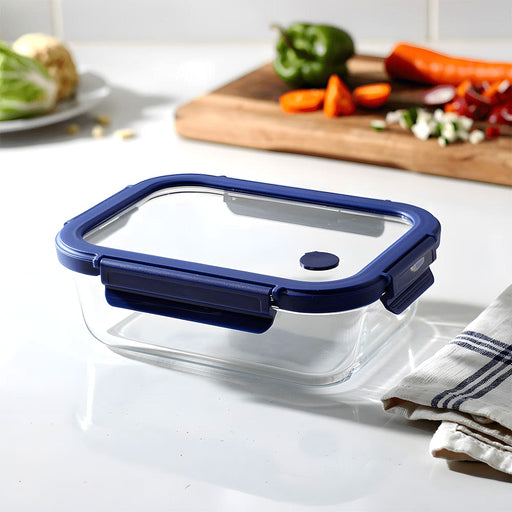Trekk Crib Glass Lunch Box - A glass lunch box with a navy blue plastic lid, placed on a kitchen counter next to fresh vegetables and a towel.