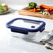 Trekk Crib Glass Lunch Box - A glass lunch box with a navy blue plastic lid, placed on a kitchen counter next to fresh vegetables and a towel.
