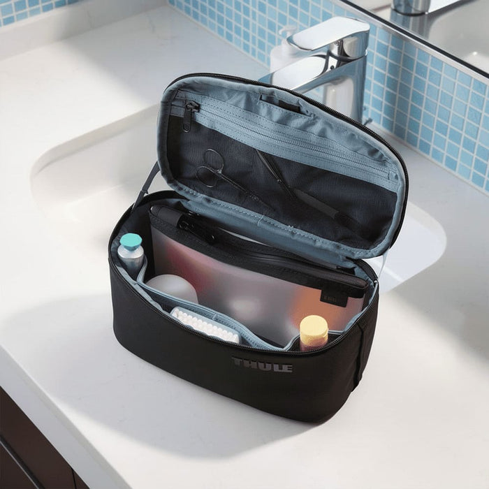 Thule Subterra 2 Toiletry Bag w/ Removable Pouch - A black toiletry bag with a removable pouch, featuring various personal care items inside, displayed on a bathroom countertop.
