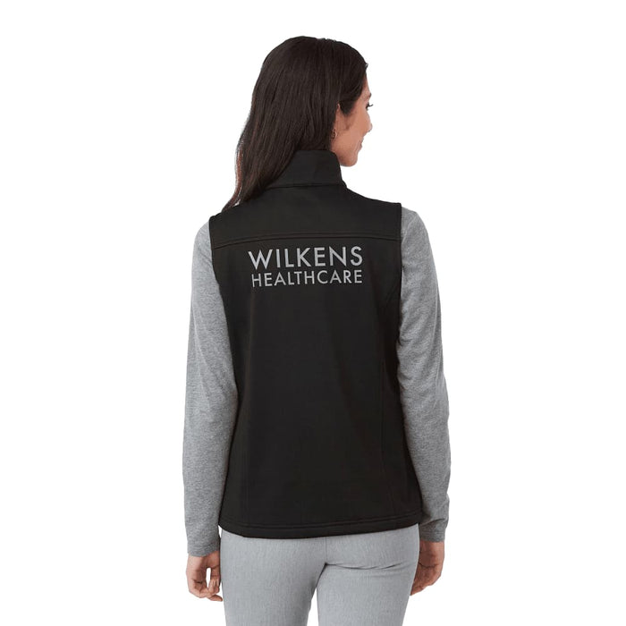 Women's Joris Eco Waterproof Softshell Vest - A black women's softshell vest with a high collar and grey long sleeves visible underneath, featuring a logo on the back.