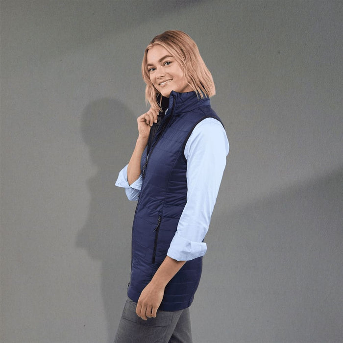 Women's Telluride Lightweight Packable Insulated Puffer Vest - A woman wearing a navy lightweight packable insulated puffer vest, paired with a light blue shirt and grey pants.