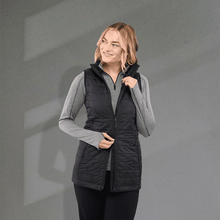 Women's Telluride Lightweight Packable Insulated Puffer Vest - A black insulated puffer vest with a zip front, worn over a grey long-sleeve top, featuring a logo.
