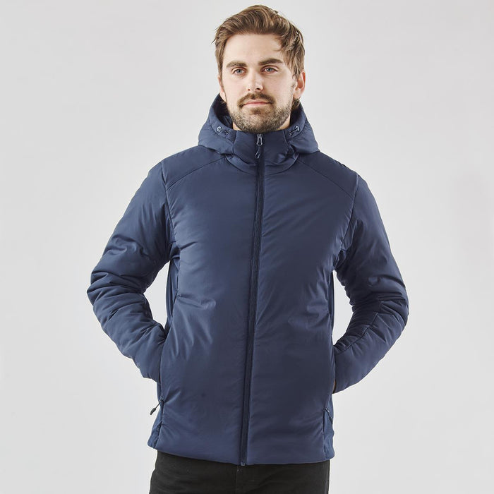 Men's Cascadia Thermal Jacket - A man wearing a navy puffer jacket with a hood, featuring a branding logo. The jacket has a sleek, modern design.